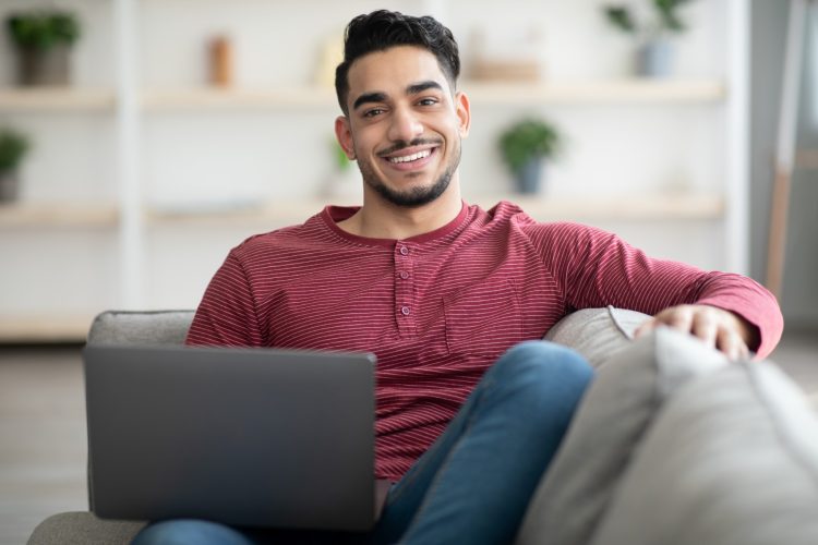smiling-arab-guy-reclining-on-sofa-with-laptop-W2DPVB2.jpg
